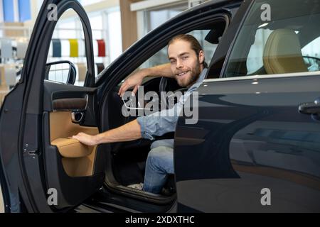 Young bearded man sitting in a car and opening a car door Stock Photo