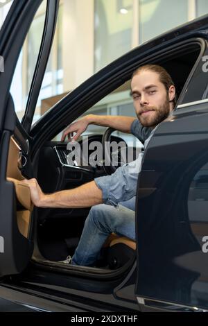 Young bearded man sitting in a car and opening a car door Stock Photo