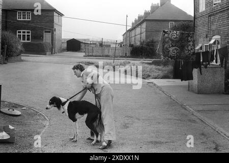 Coal mining pit village Yorkshire UK 1970s. A woman walks her dog in the Northfield Estate, which comprised of National Coal Board (NCB) houses. A carpet and clothes hang up outside a house to dry on the washing line that stretches across the road. South Kirkby, Yorkshire England 1979 HOMER SYKES Stock Photo