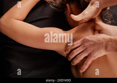 a male masseur massages a girl's neck on a dark background, neck