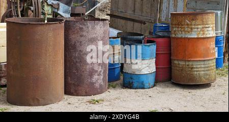 Rusty iron barrels stand on the ground near a village fence panorama Stock Photo