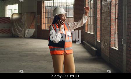 Black Female Engineer Inspecting Construction Site and Talking on Phone Stock Photo