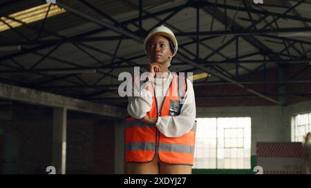 Female Architect in a Construction Site Wearing Safety Gear and Reflecting on Future Projects Stock Photo