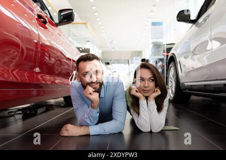 A cheerful married couple lies on the floor of a car dealership choosing a new car with a smile on their faces Stock Photo