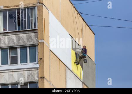 TULA, RUSSIA - OCTOBER 10, 2020: Industrial climber worker applying additional styrofoam insulation on outside wall of nine-stor Stock Photo