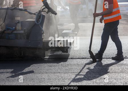 Men working with asphalting paver machine during road street repairing works at day light with smoke and steam in the air Stock Photo