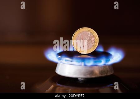 Gas stove burner with one euro coin standing vertically on top, burning natural gas with blue flame Stock Photo