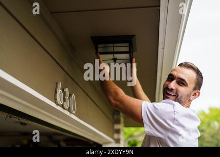 Electrician man hand holding multi meter and checking voltage at the electrical terminal, replacement LED lamp at home outdoor. Maintenance concept. Stock Photo