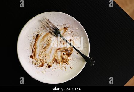 Top view empty fork and dish with stains of chocolate and cake after eating. Food dish is on black table with space. Stock Photo