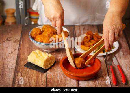 Woman in white apron serving meatballs in an earthenware pot Stock Photo