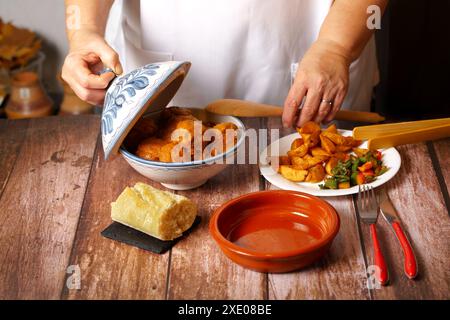 Woman in white apron serving meatballs in an earthenware pot Stock Photo
