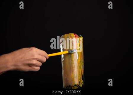 A glass bottle being painted with a yellow brush. Isolated on black background. Stock Photo