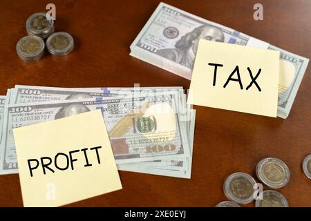 A stack of money says tax on it. Big taxes on small profits, concept. Office stickers on dollar bills on wooden table Stock Photo