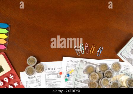 A table with a calculator, a stack of papers, and a pile of coins.  US tax form 1042 S with note and pen. tax form. law document usa. pink background. Stock Photo