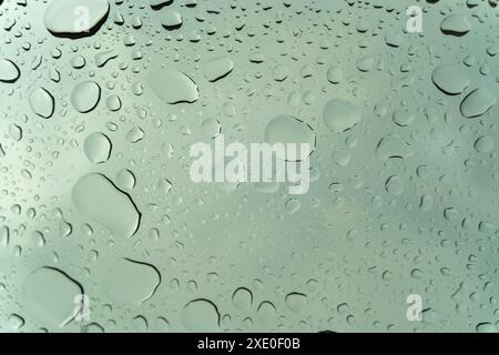 A window with raindrops on it. The raindrops are scattered all over the window, creating a blurry and hazy effect. Scene is calm and peaceful, as the Stock Photo