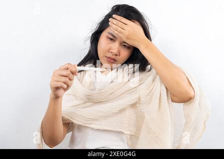 A young woman lies in bed and blows her nose into a handkerchief, takes her temperature and reaches for the pills with her hand. Self-isolation and si Stock Photo