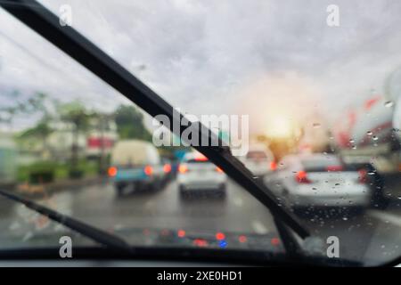 A car windshield is covered in raindrops and the wipers are in motion. The scene is a busy city street with many cars and trucks. Scene is chaotic and Stock Photo