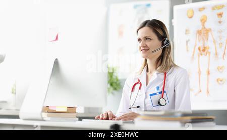 Smiling female doctor consultant in headphones is providing medical assistance remotely Stock Photo
