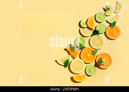 Creative background made of summer tropical citrus fruits, orange, tangerine, lemon, lime and mint leaves on yellow background, copy space. Trendy foo Stock Photo