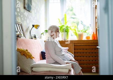 Elderly woman sitting alone on a bed in nursing home Stock Photo