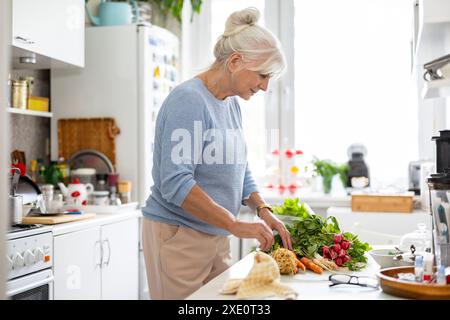 Senior woman preparing vegetable salad in kitchen at home Stock Photo