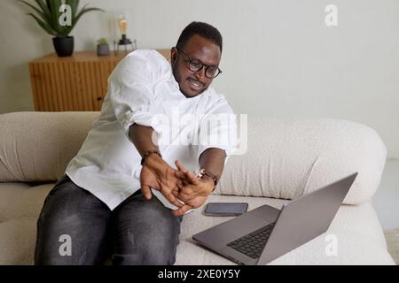 Young businessman stretches his hands after a long time working on a laptop in a cozy home, working online Stock Photo