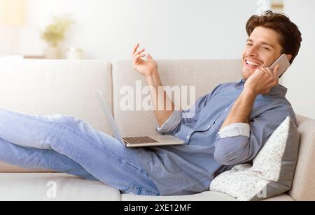 Man on Couch Talking on Phone With Laptop Stock Photo