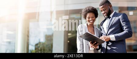 Happy couple of african american business partners working while standing outdoors, discussing new project. Blurred background with copy space Stock Photo