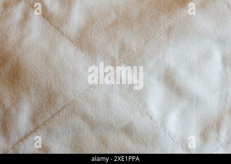 Close-up of a quilted fabric texture made of cotton with a meticulously crafted diamond pattern and uniform stitching showcasing natural discoloration Stock Photo