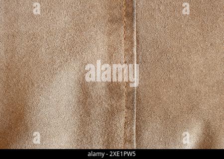 Close-up of a beige textured fabric  with vertical seam, showcasing its fine, soft surface and precise seams, highlights the fabric’s luxurious textur Stock Photo
