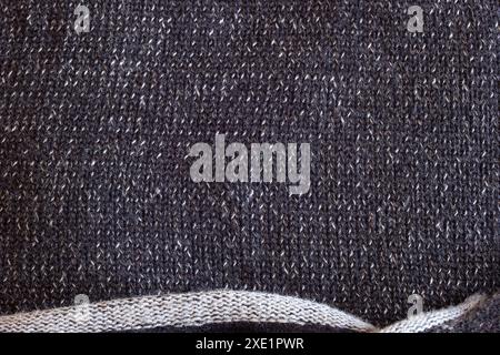 Close up of a sweater with  white and dark gray threads creates a monochromatic depth. The bottom edge, with its sparse weave and raw finish. Stock Photo