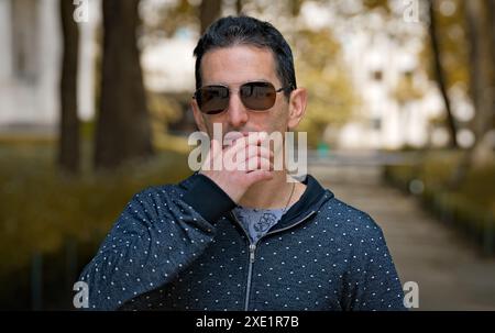 Mediterranean man in casual sports clothing and sunglasses, focused attitude with a hand on the face. Stock Photo