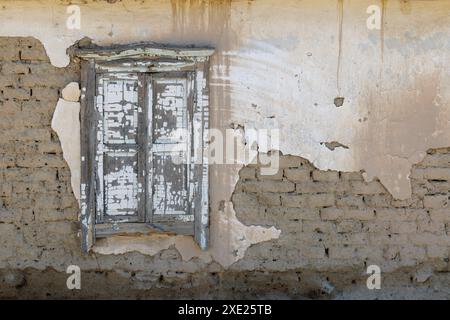 Old adobe building wall with old shabby closed wooden window and peeled off plaster Stock Photo