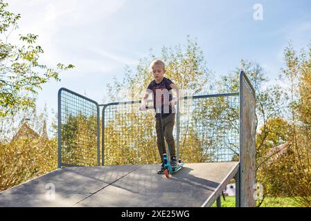 Child on kick scooter in park. Kids learn to skate roller board. Little boy skating on sunny summer day. Outdoor activity for ch Stock Photo