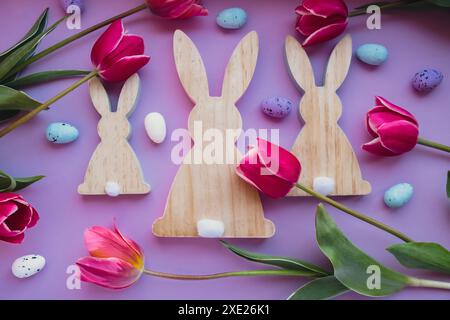 Easter eggs and wooden bunnies with pink tulips on violet pastel background. Flat lay composition, top view. Decoration minimali Stock Photo