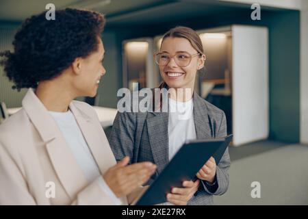 Young female sales managers standing in modern coworking and using digital tablet together Stock Photo