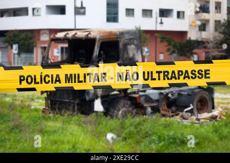 Truck burnt by a pyromaniac with a police tape with written in it in Portuguese 'Polícia militar - Não ultrapasse' meaning in English 'Military police Stock Photo