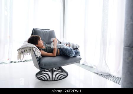The boy lies in a chair and reads. Stock Photo