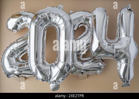 Silver foil number 2024 celebration new year balloon on neutral beige background. Happy New year greetings concept. Two thousand Stock Photo