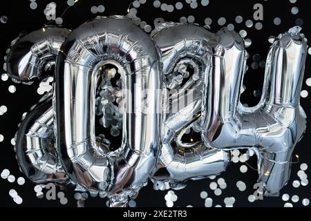 Happy new year 2024 metallic balloons with confetti on dark black background. Greeting card silver foil balloons numbers Christm Stock Photo