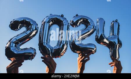 Silver foil number 2024 celebration new year balloon on blue sky background. Happy New year greetings concept. Hands holding bal Stock Photo