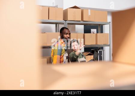 Diverse warehouse managers packing parcels and managing delivery operations. Colleagues working in post office storage, standing beside cardboard boxes shelves preparing orders in storage room Stock Photo