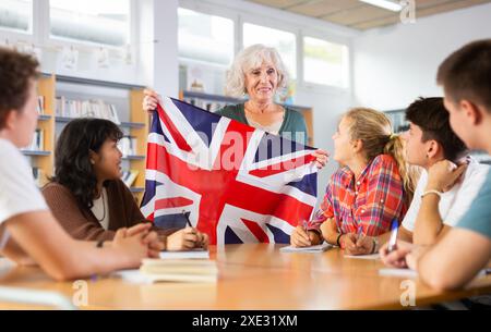 Elderly teacher shows the flag of Great Britain to teenagers and talks about this country during lesson at library school Stock Photo