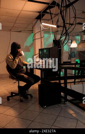 Young man working on security breach hacking, committing cyberterrorism and stealing personal data. causing computer malware at night. Online criminal cracking server encryption. Stock Photo