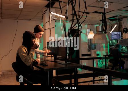 Hackers group coding internet virus program, developing malicious software, criminals stealing privacy information. Cybercrime, scammers hacking computer system, breaking into database at night time Stock Photo