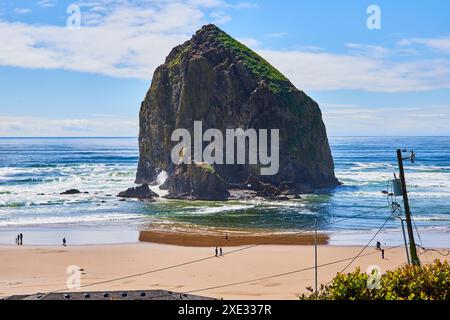 Haystack Rock with Ocean Waves and Beach Walkers from Elevated View Stock Photo