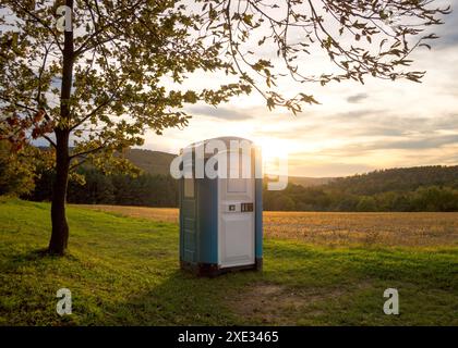 Blue plastic toilet cabin in woodland at sunset Stock Photo