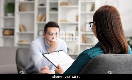 Female psychologist listening to her depressed male patient and taking notes, mental health and counseling concept. Stock Photo