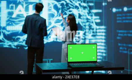 Teamworking AI technicians using green screen laptop for business data analysis. Team of IT experts works on mockup notebook to automatize tasks using artificial intelligence, camera A Stock Photo