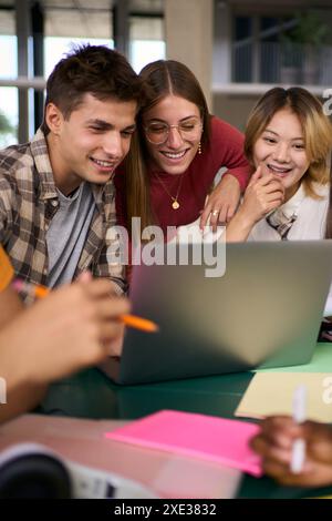 Three young university students people gathered using laptop together in campus study hall. Stock Photo